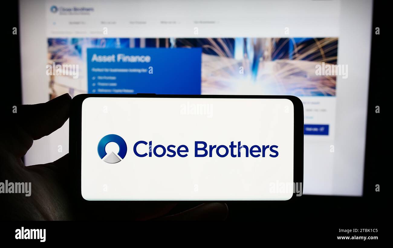 Person, die ein Mobiltelefon mit dem Logo der britischen Handelsbank Close Brothers Group plc vor der Webseite hält. Schwerpunkt auf dem Display des Telefons. Stockfoto
