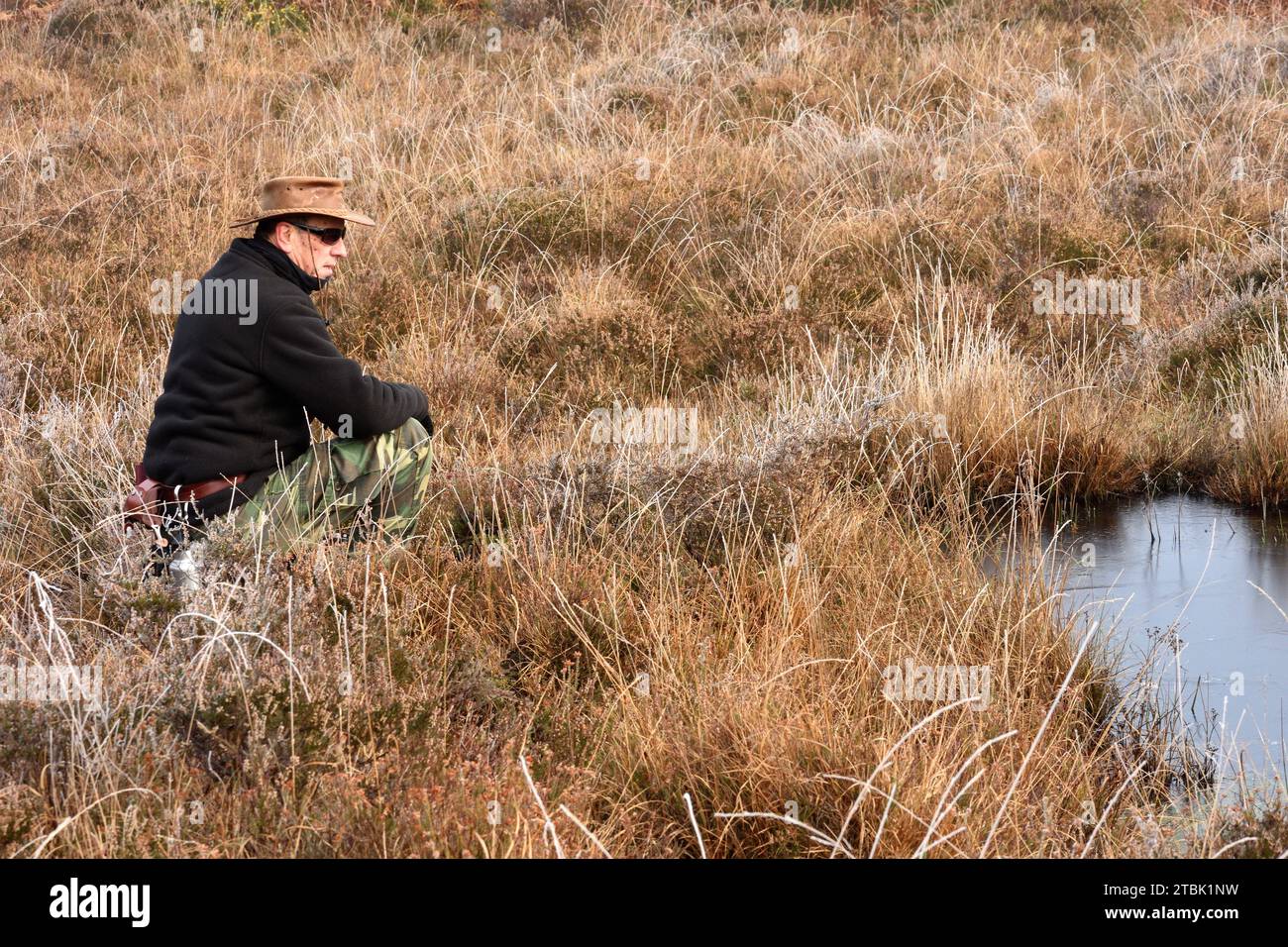 Mann mit Hut hockt im Herbstsumpfland bei Dogwood Bottom, New Forest UK Stockfoto