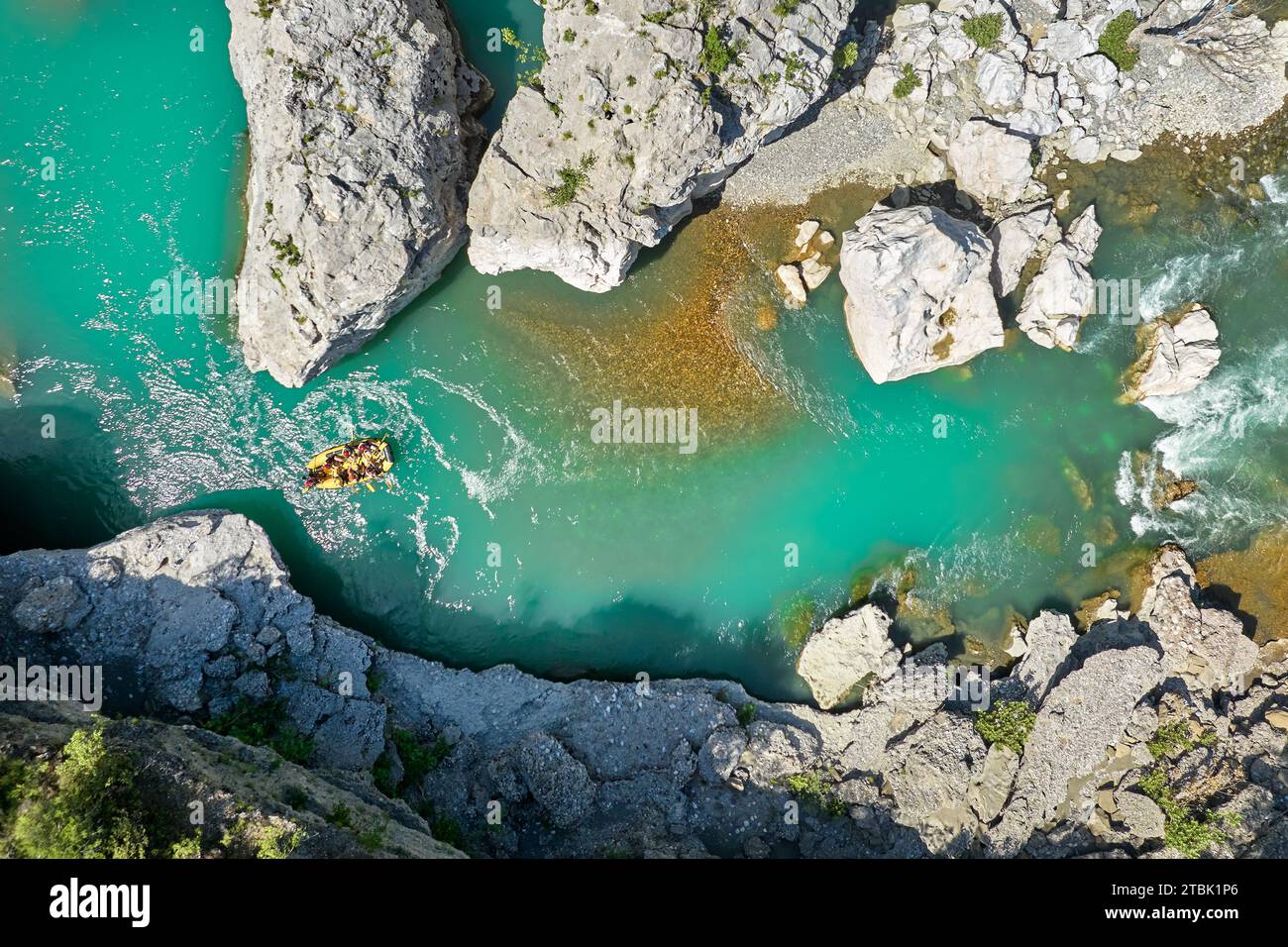 Wildwasser-Rafting. Abenteuer und Sport. Ein gelbes Floß schwimmt zwischen den Felsen auf dem kristallklaren, blau-grünen Wasser. Rechtwinklige Drohnenansicht. Stockfoto