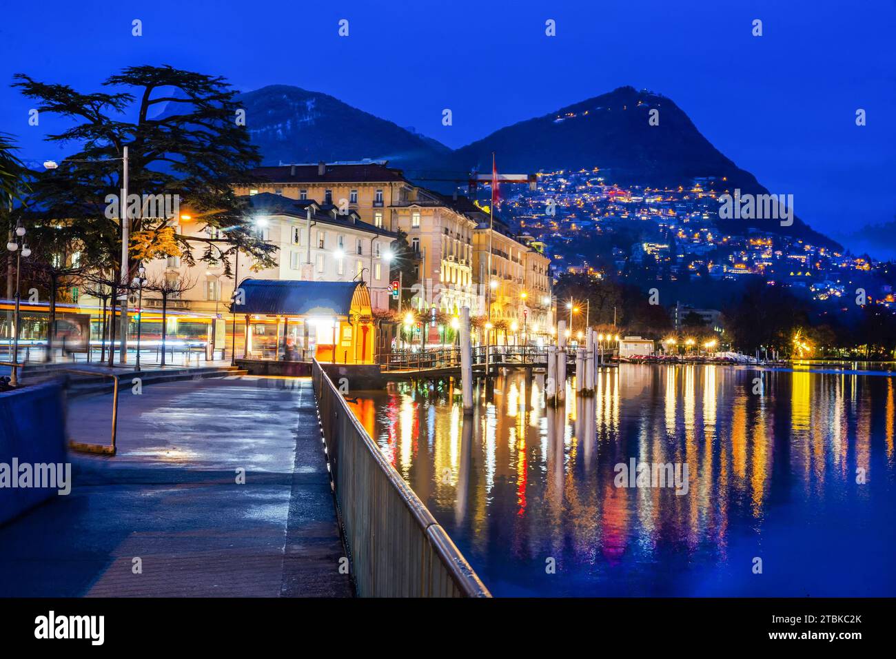 Fantastischer Blick auf die beleuchtete Stadt Lugano, den Damm Giocondo Albertoll, den Berg Bre, das Kasino (?) Bukilding. Reflexionen im Wasser des Luganer Sees Stockfoto