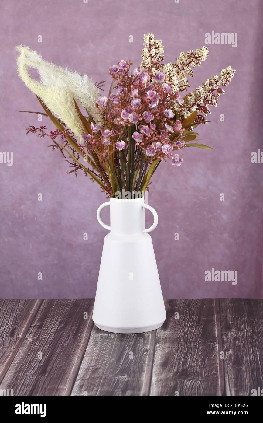 Künstliche Blumen in weißer Vase auf rosa Stoffhintergrund. Stockfoto