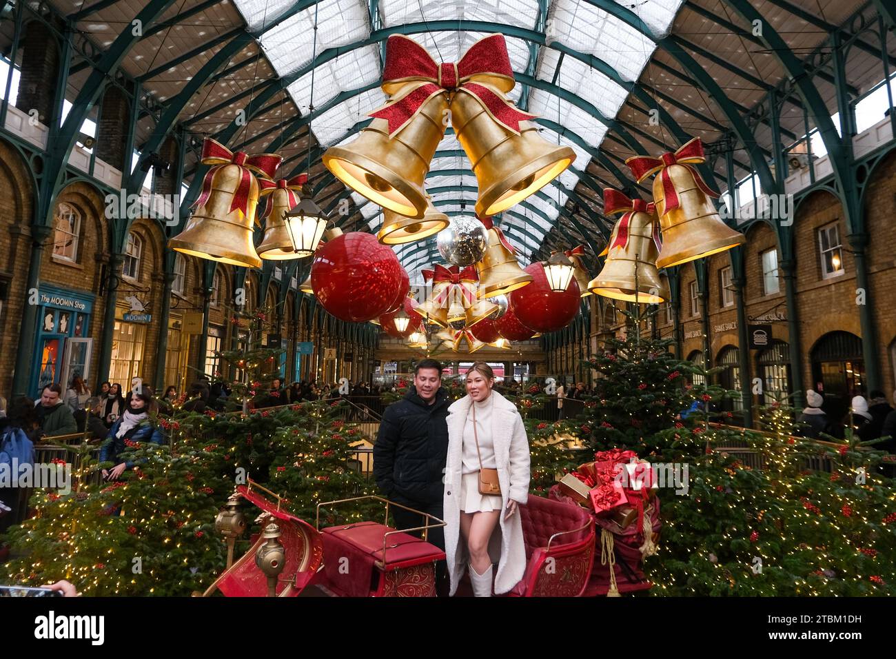 London, Großbritannien. Ein Paar posiert für ein Foto auf dem Apple Market von Covent Garden, der mit festlichen Riesenglocken und Kugeln dekoriert ist. Stockfoto