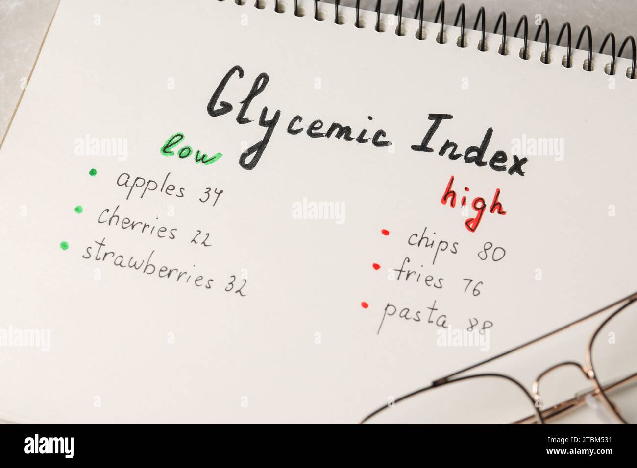Liste mit Produkten mit niedrigem und hohem glykämischen Index in Notizbuch auf Tabelle, Nahaufnahme Stockfoto