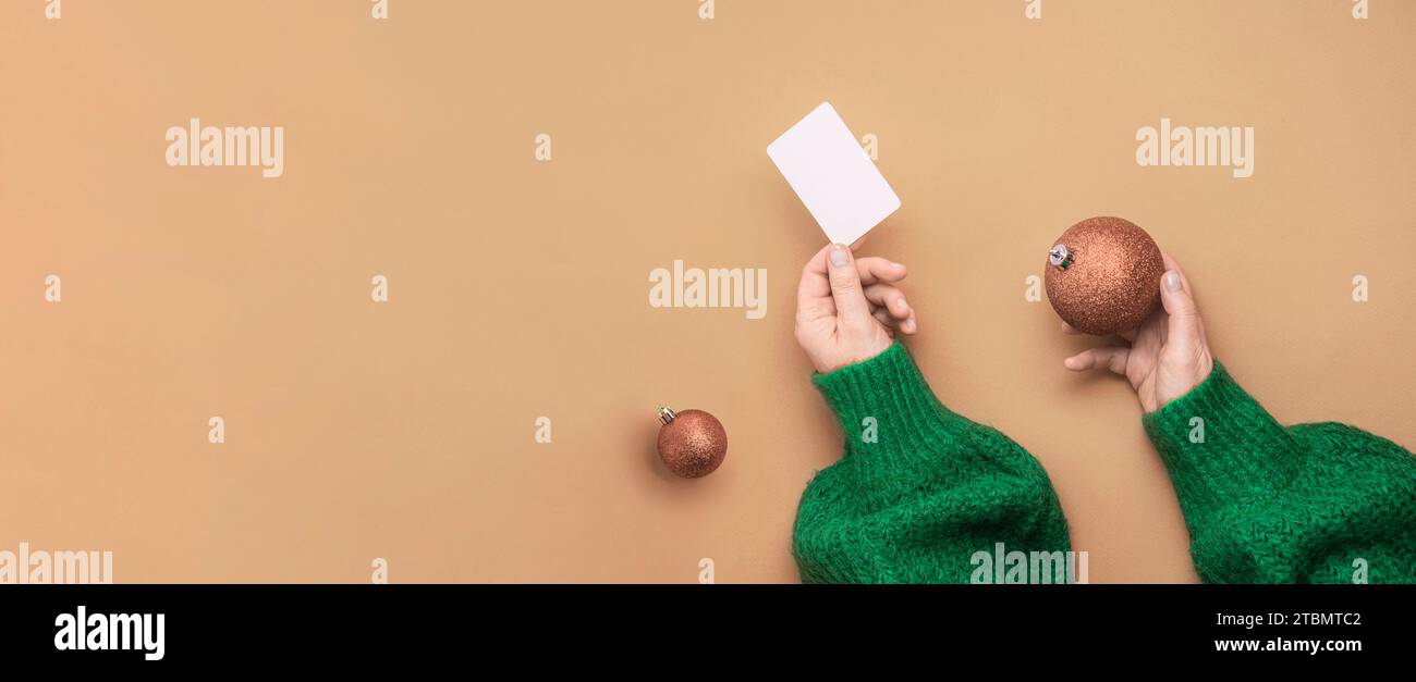 Weihnachtseinkaufskonzept. Flache Hände in einem grünen Pullover mit Bonuskarte. Banner auf rotem Hintergrund Stockfoto