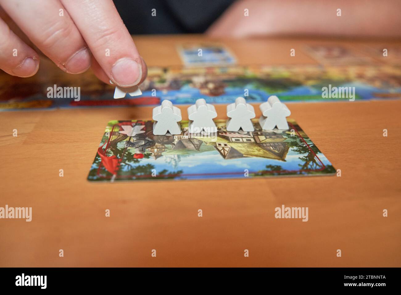 Hand hält die weiße Holzfigur auf dem Brettspiel und legt sie auf das Brett Stockfoto