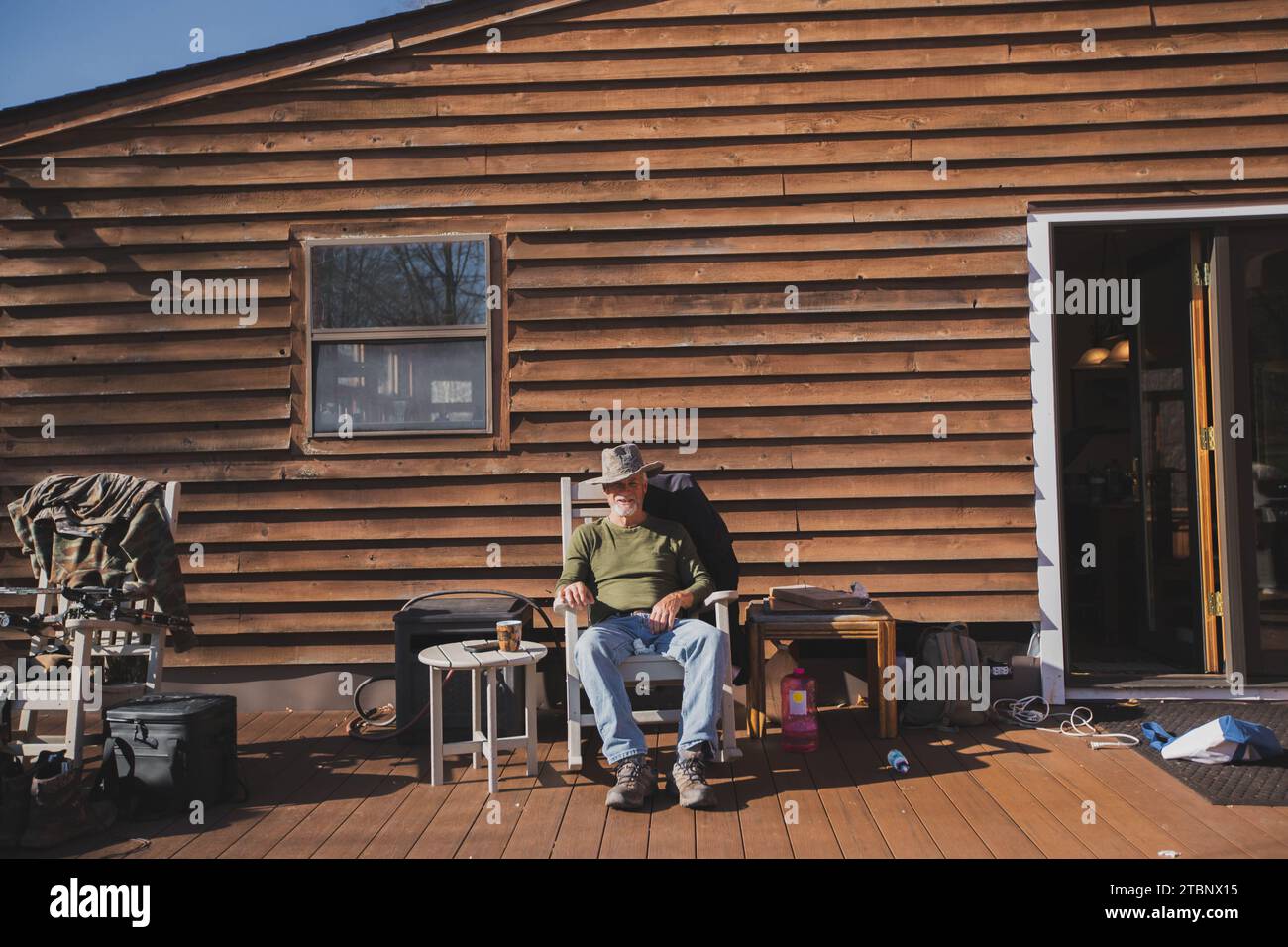 Mann in Cowboy Hut, der im Schaukelstuhl auf der Veranda einer Holzhütte sitzt Stockfoto