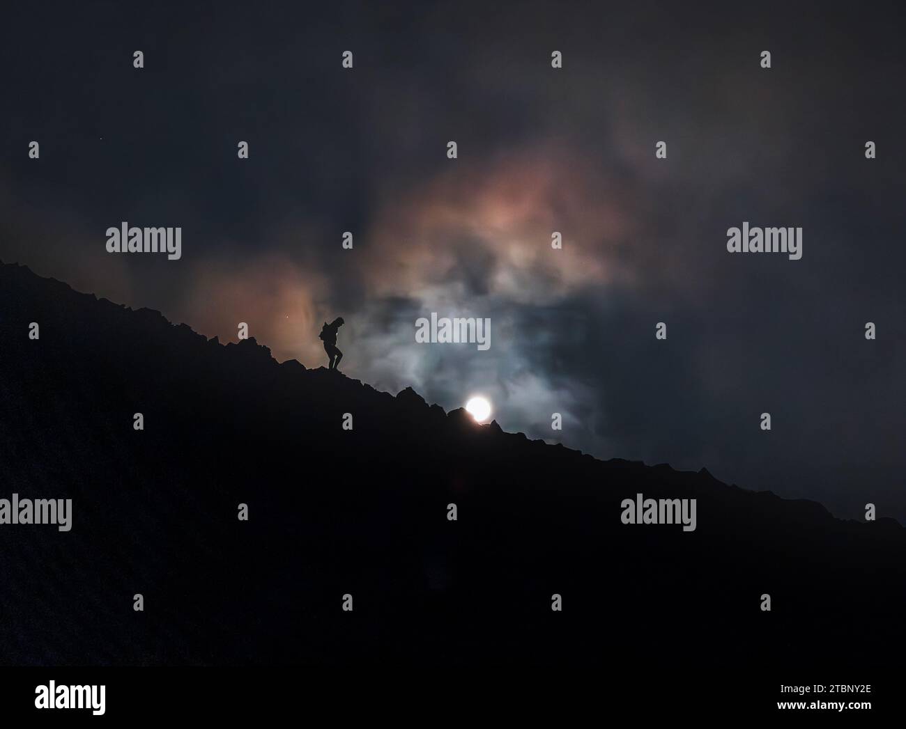 Der Mensch läuft nachts auf dem Bergrücken mit Vollmond und Wolken Stockfoto