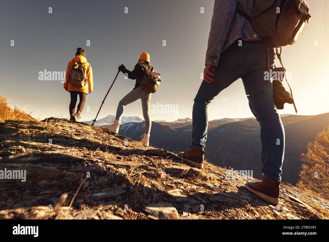 Drei junge Touristen oder Wanderer mit Rucksäcken stehen am Aussichtspunkt und blicken auf den Sonnenuntergang Stockfoto