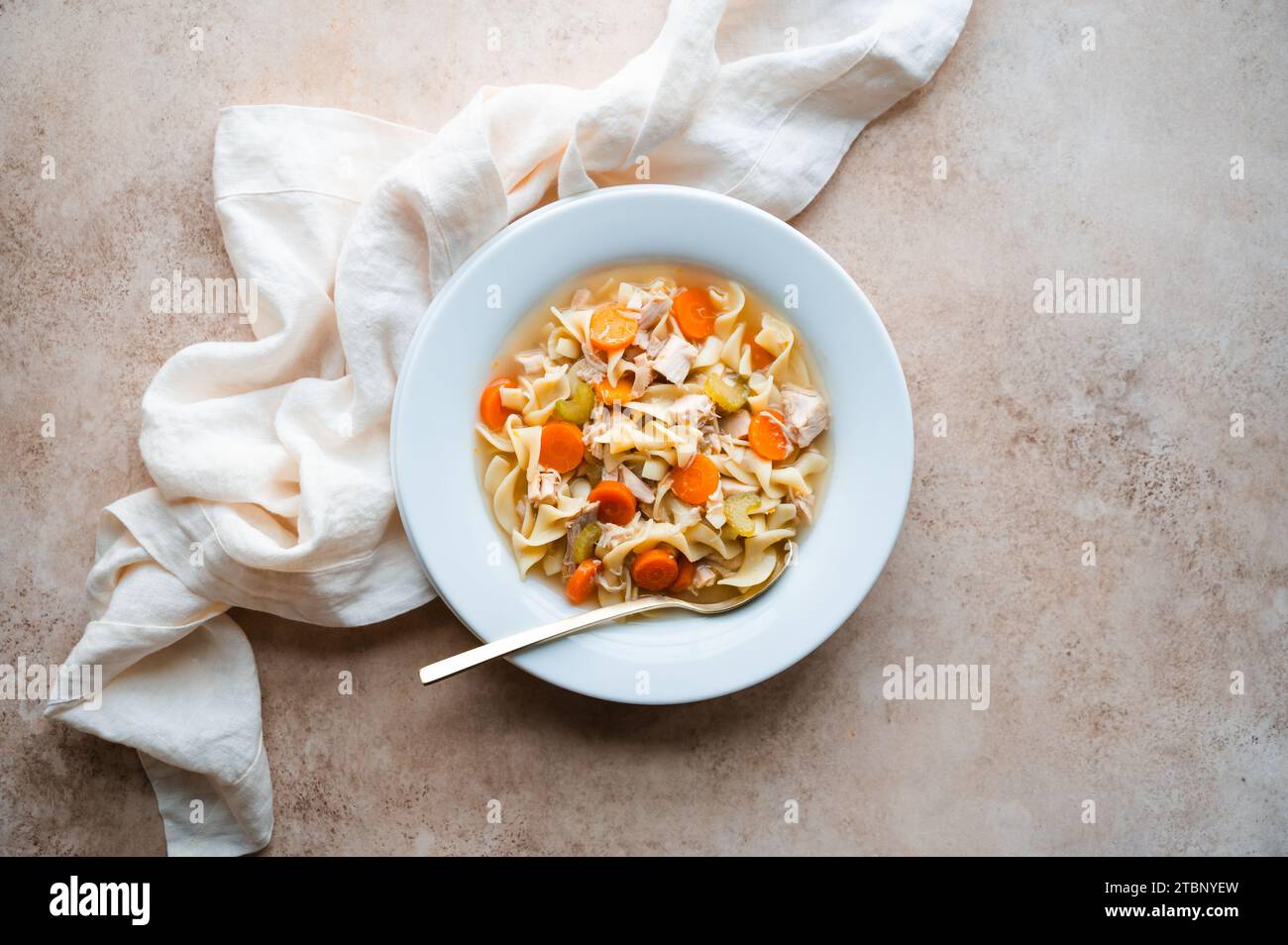 Hähnchennudelsuppe mit Blick von oben in einer weißen Schüssel auf beigem Hintergrund. Stockfoto