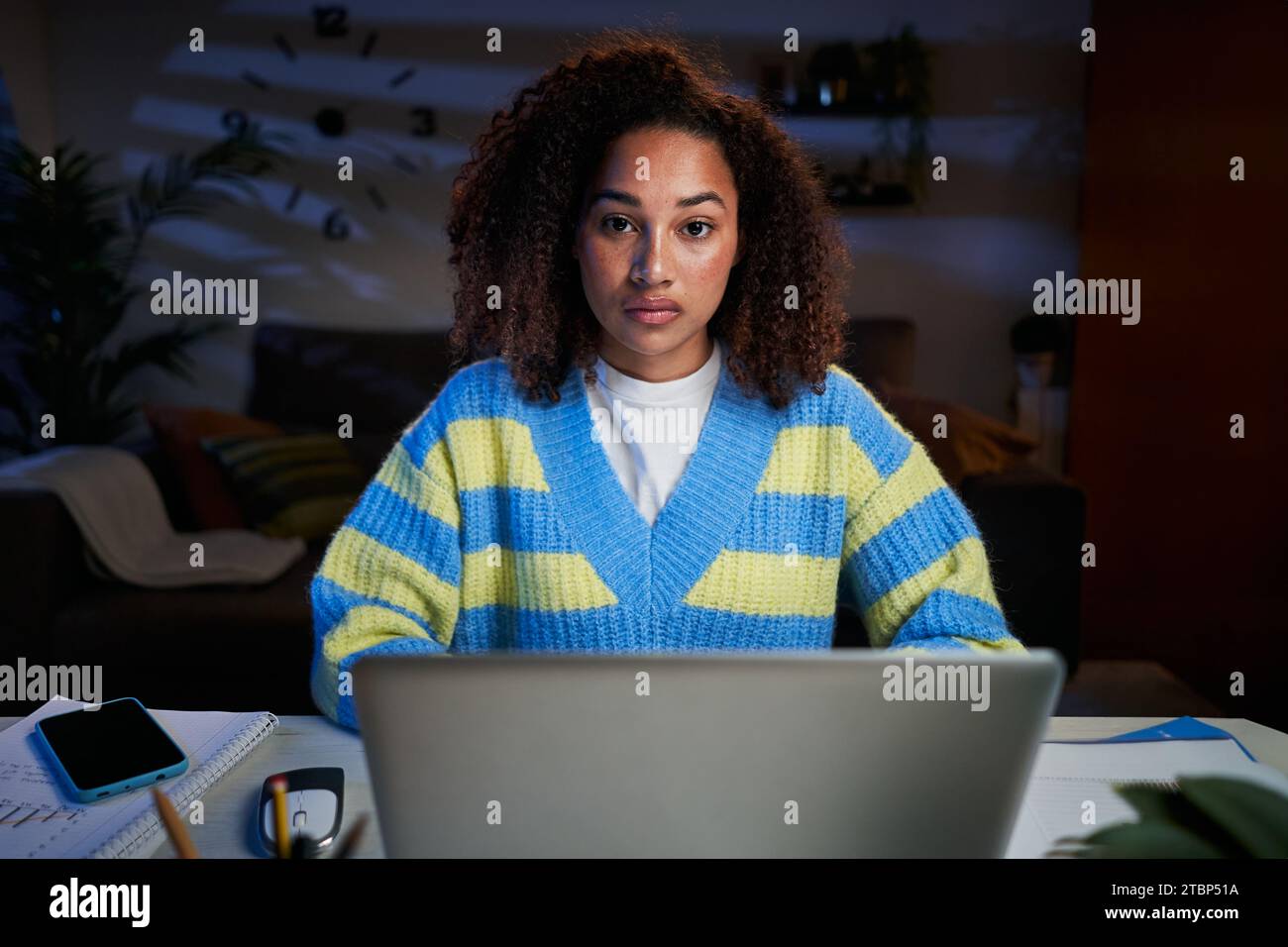Porträt ernste junge Afro-Frau, die konzentriert auf die Kamera blickt, die vor dem Laptop zu Hause sitzt. Stockfoto