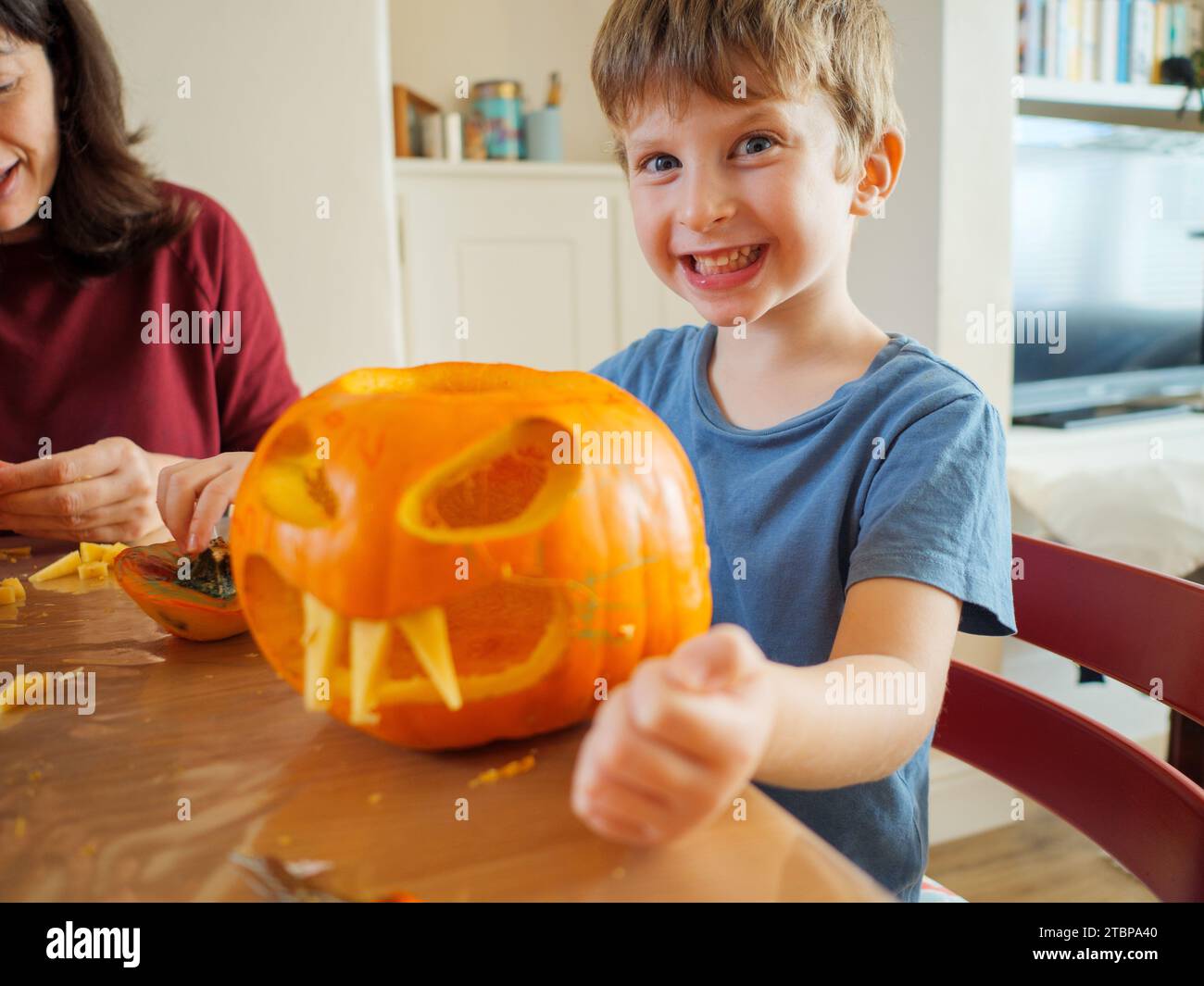 Lächelndes, glückliches kleines Kind, das Spaß daran hat, Gruselgesicht-Kürbis zu machen, um halloween zu Hause, Großbritannien, zu feiern Stockfoto