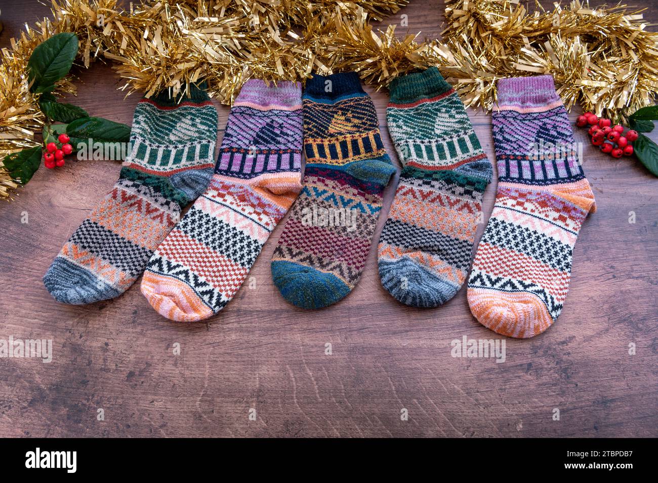 Eine Reihe farbenfroher Wintersocken aus Wolle mit Weihnachtsdekoration auf Holzhintergrund. Stockfoto