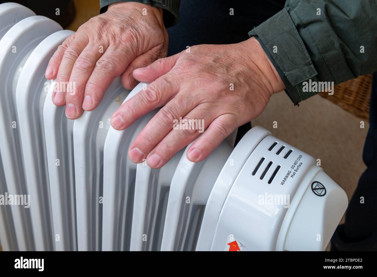 Nahaufnahme einer Person, die die Hände auf eine tragbare elektrische Heizung legt, um sie auch im Winter warm zu halten. Stockfoto
