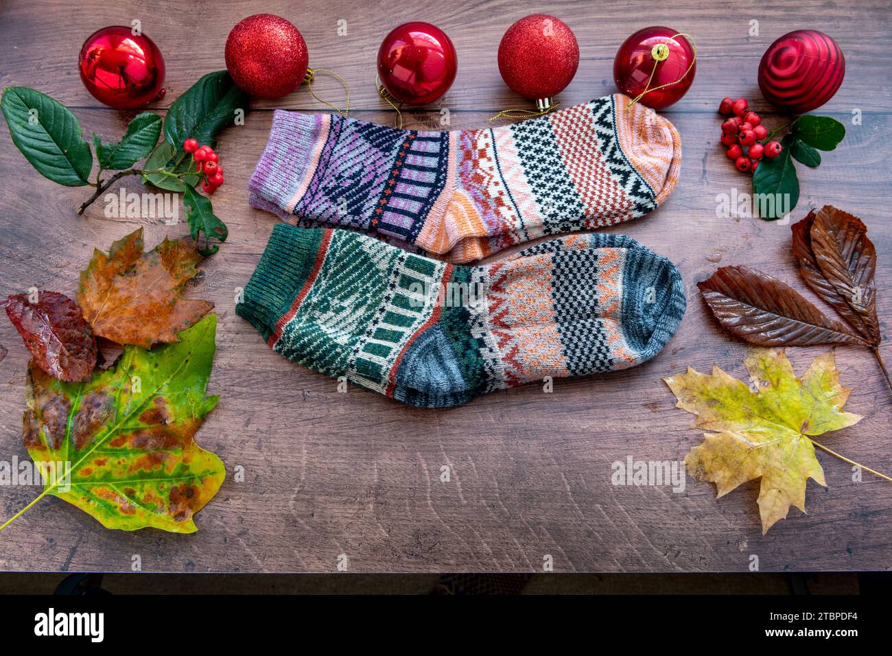 Zwei Paar farbenfrohe Wintersocken aus Wolle mit Weihnachtsdekoration und gefallenen Blättern auf Holzhintergrund. Stockfoto