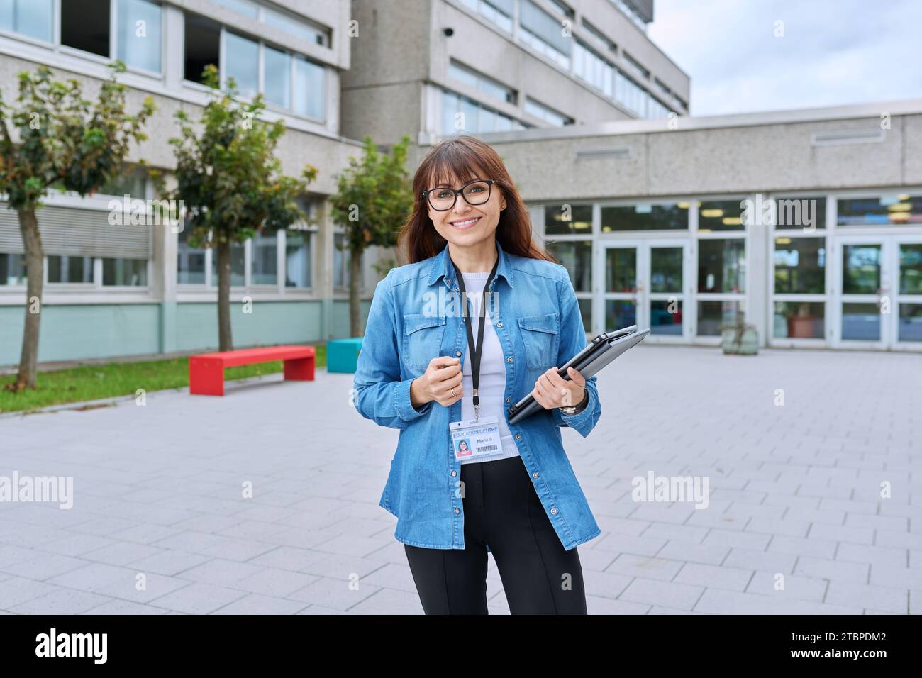 Schullehrerin mittleren Alters mit digitalem Tablet posiert in der Nähe des Schulgebäudes Stockfoto