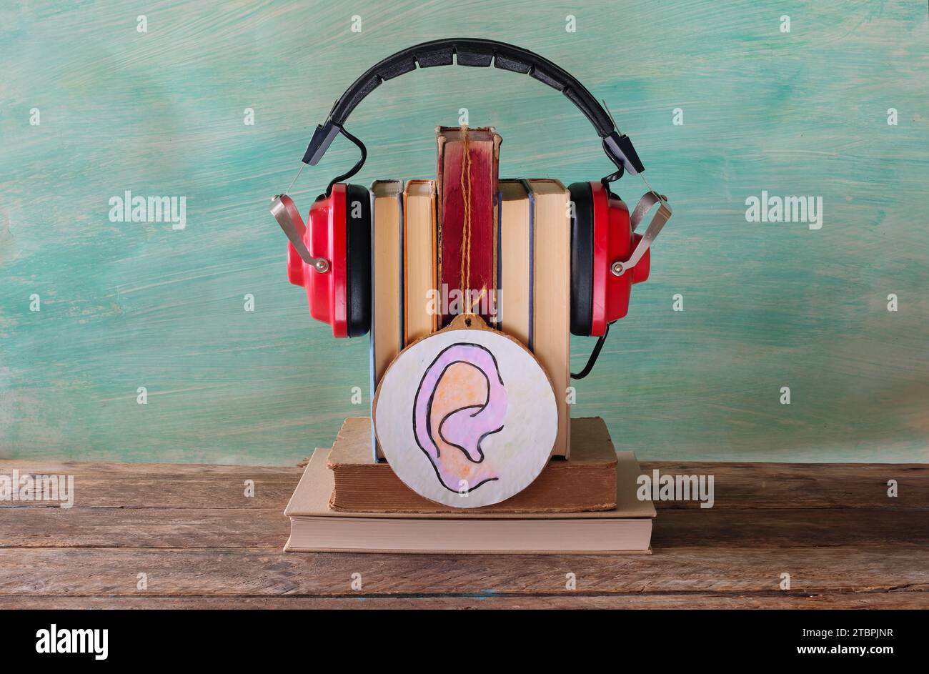 Hörbuchkonzept mit Bücherstapel, Vinatge-Kopfhörer und Zeichnung eines menschlichen Ohres, freier Kopierraum Stockfoto