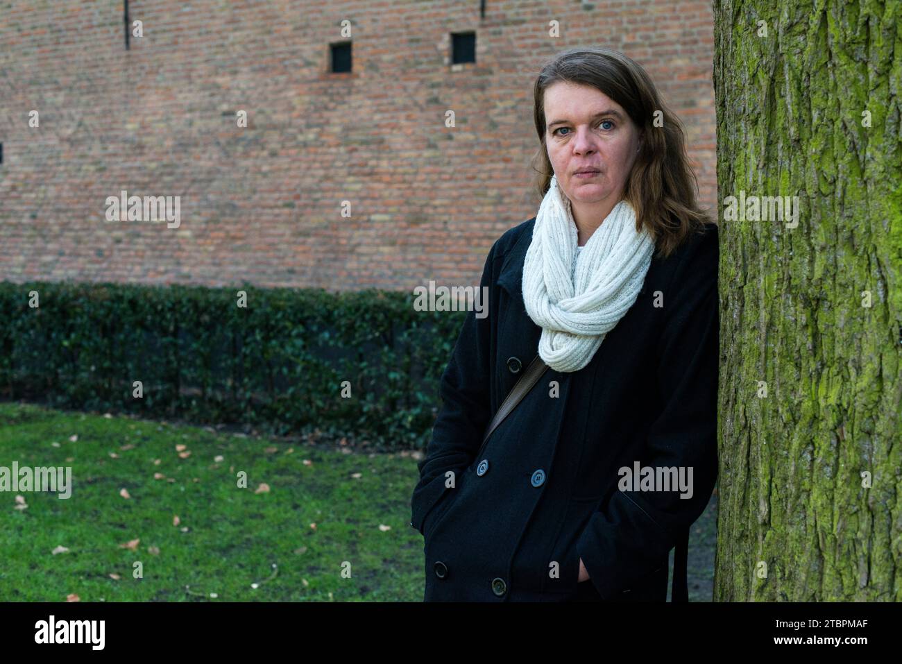 Breda, Niederlande. Porträt einer mittelerwachsenen kaukasischen Frau, die sich an den Baum eines Stadtparks lehnt. Stockfoto