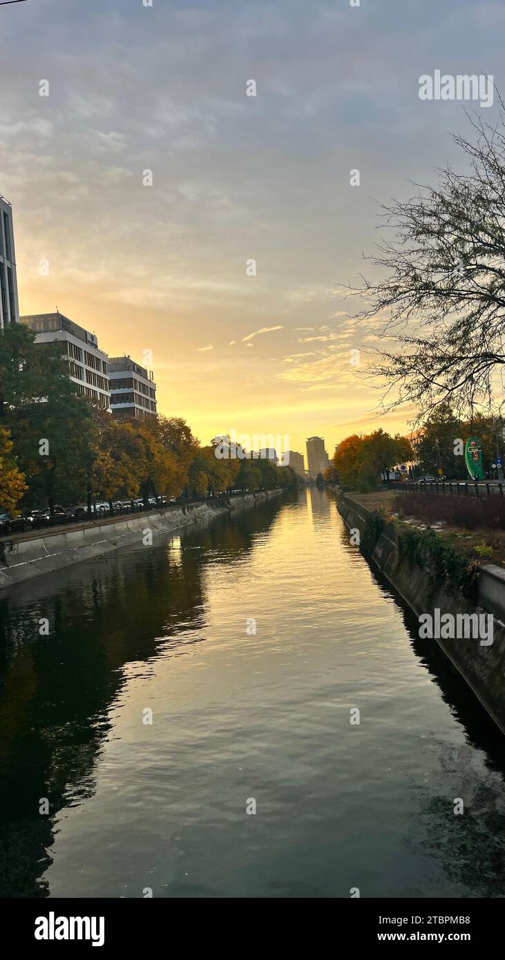 Eine beeindruckende Szene mit einem spektakulären Sonnenuntergang über einem ruhigen Fluss, das stille Wasser glitzert im warmen, orangen Licht der untergehenden Sonne Stockfoto