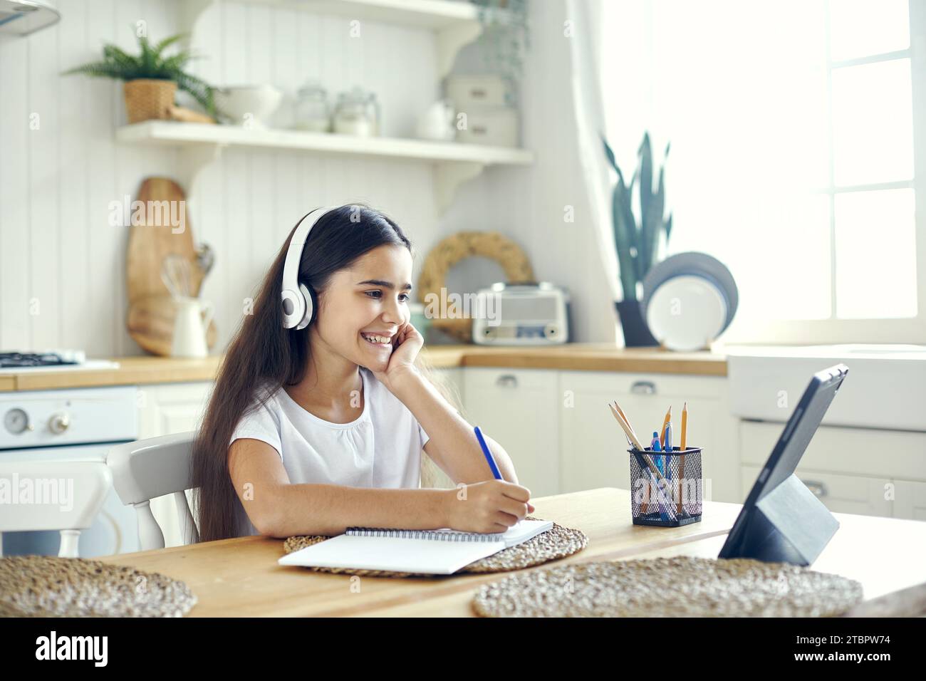 Hübsches Mädchen aus den 12er Jahren mit schnurlosen Kopfhörern sitzt am Tisch e-Learning, hört Online-Kurse, Hörunterricht, erhaltet neues Wissen und Fähigkeiten mit Inte Stockfoto