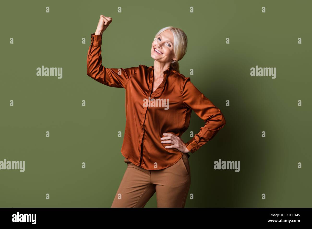 Foto-Porträt der attraktiven Rentnerin Frau Fäuste Muskeln selbstbewusst gekleidete stilvolle seidenbraune Kleidung isoliert auf khakifarbenem Hintergrund Stockfoto