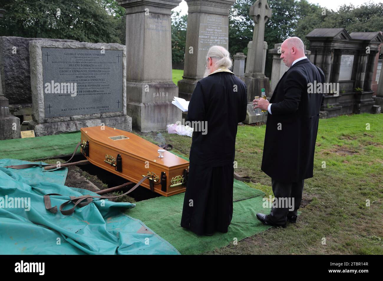 Glasgow Schottland Griechisch-orthodoxe Beerdigung in Glasgow Necropolis - Priester liest die verbindlichen Gebete auf der Grabstätte mit dem Trauerdirektor Holding Olive Stockfoto