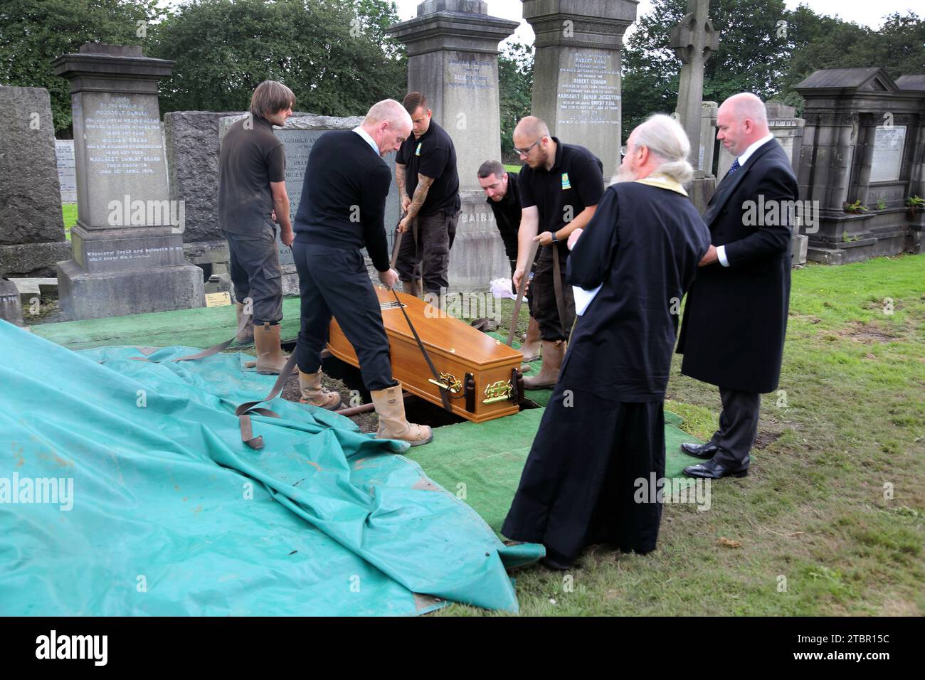 Glasgow Schottland Griechisch-orthodoxe Beerdigung in Glasgow Necropolis - Priester, der den Committal Service durchführt, während der Sarg manuell in die GRA abgesenkt wird Stockfoto
