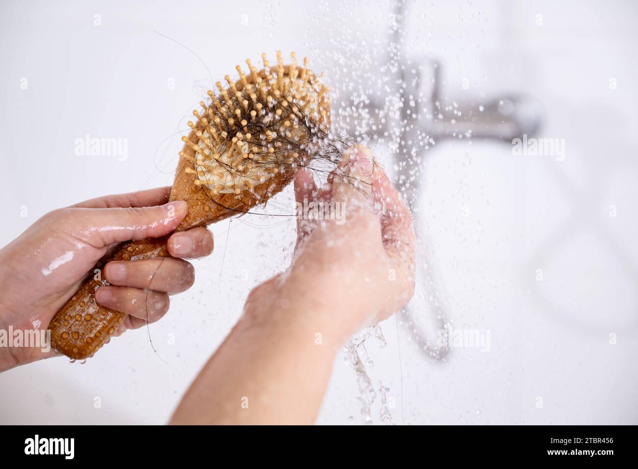 Eine Frau, die unter Alopezie leidet, sieht beim Duschen Haare auf einem Kamm Stockfoto