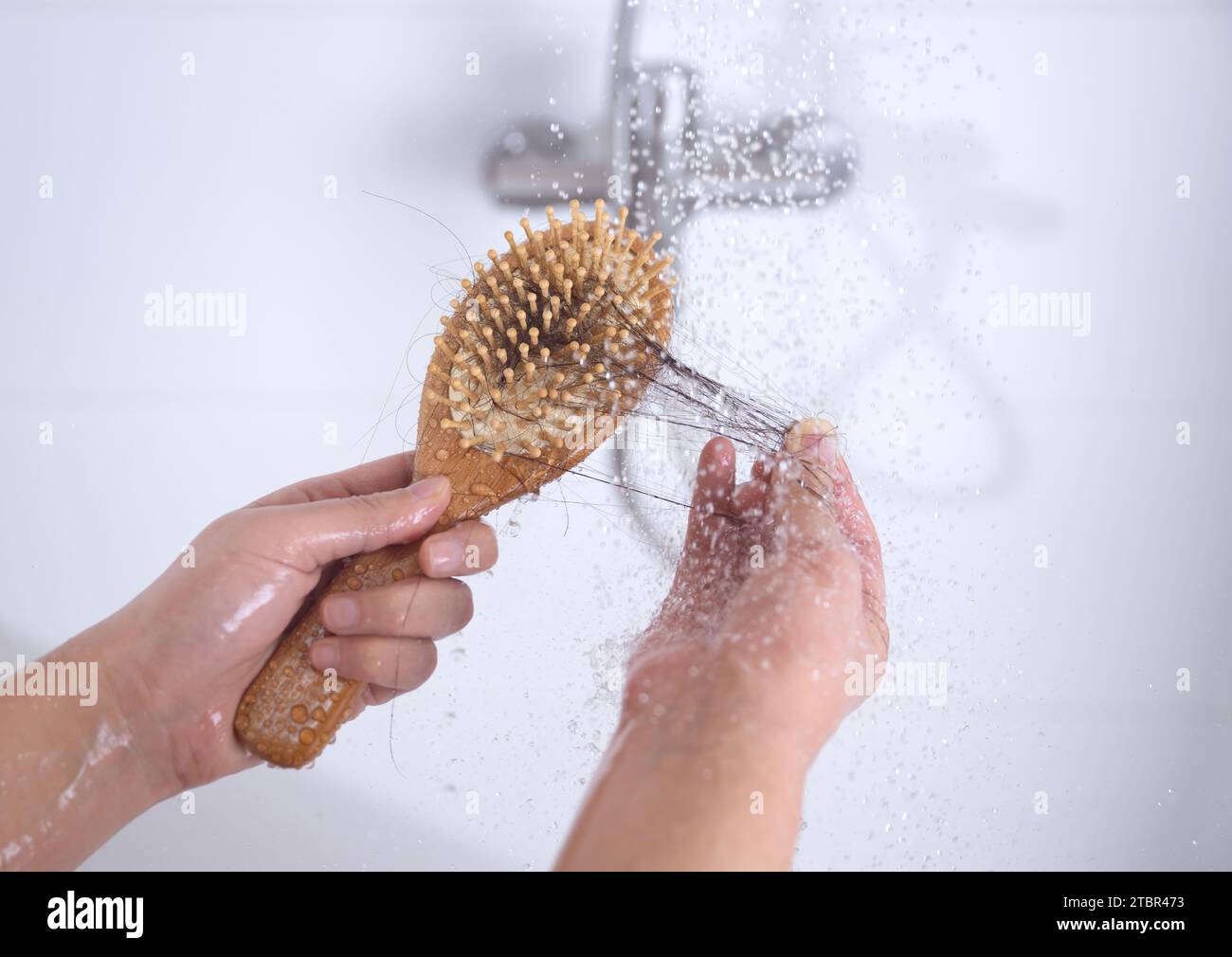 Eine Frau, die unter Alopezie leidet, sieht beim Duschen Haare auf einem Kamm Stockfoto