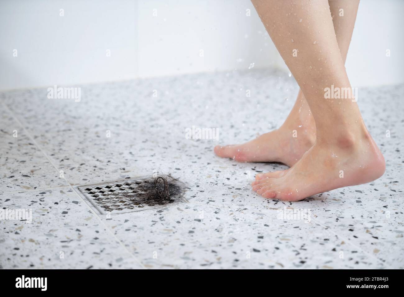 Eine Frau, die unter Alopezie leidet, duscht, im Abfluss sind Haare neben ihren Füßen Stockfoto