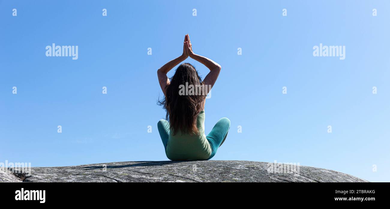 Frau in Yoga posiert auf einem Felsen unter blauem Himmel Stockfoto