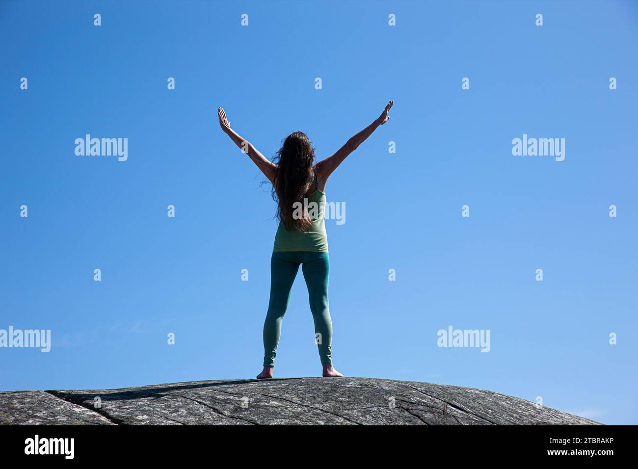 Frau mit ausgestreckten Armen isoliert auf einem Berggipfel unter blauem Himmel Stockfoto