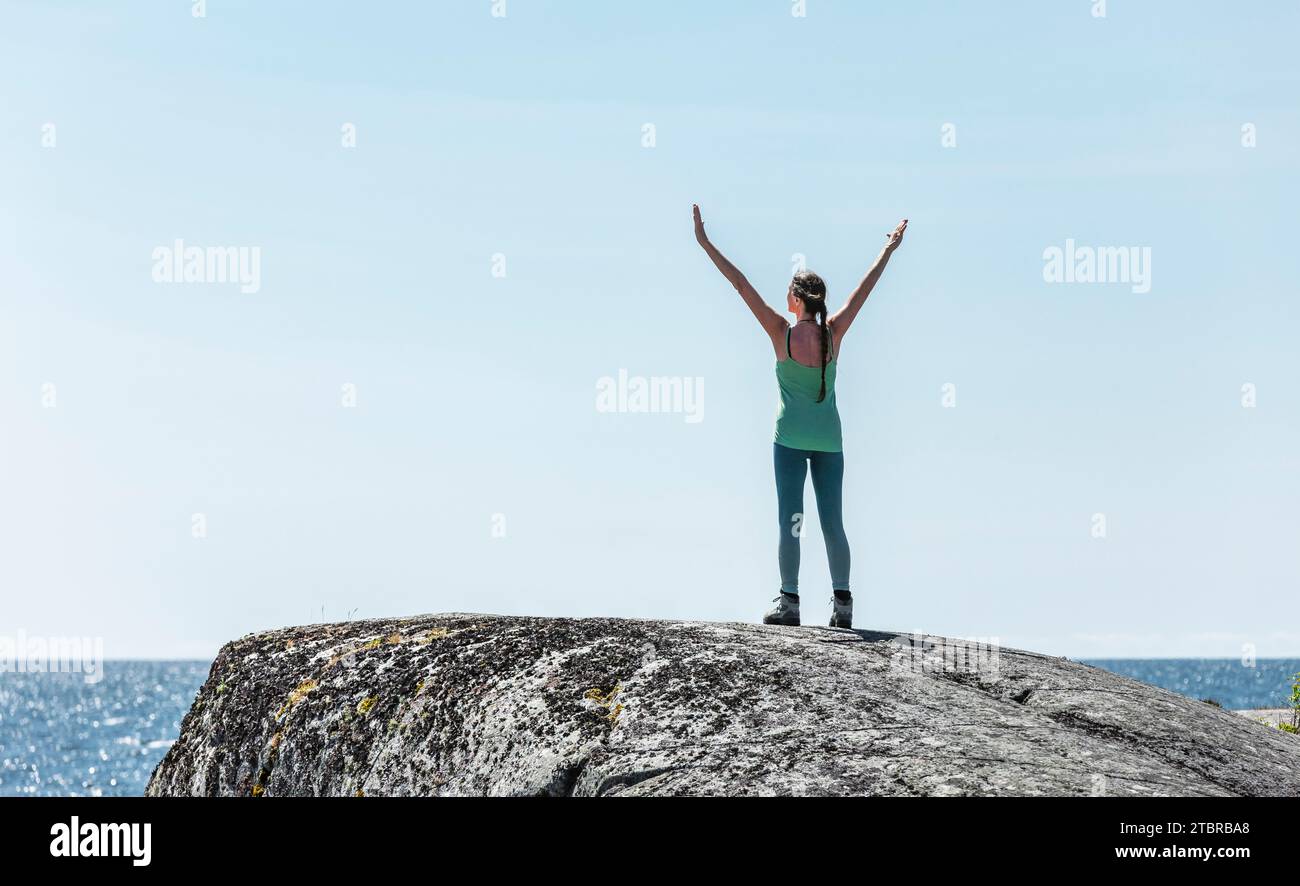 Frau mit ausgestreckten Armen auf einem felsigen Gipfel am Meer Stockfoto