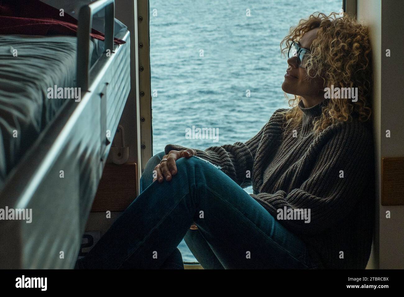 Eine Frau Passagier in der Kabinenboot Kreuzfahrt Fähre, die sich entspannt am Fenster mit Meer im Hintergrund draußen. Freizeitaktivitäten im Schlafzimmer. Menschen- und Reisekonzept. Urlaub. Stockfoto