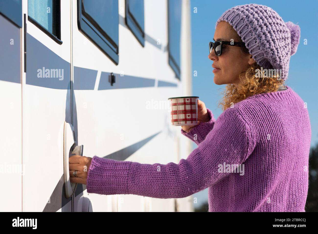 Eine hübsche Frau öffnet die Tür ihres Wohnwagens und ist bereit, alleine zu reisen. Empowerment weibliche Menschen, die ein wohnmobil fahren. Allein touristische Dame mit violettem Pullover in Wohnwagen Stockfoto