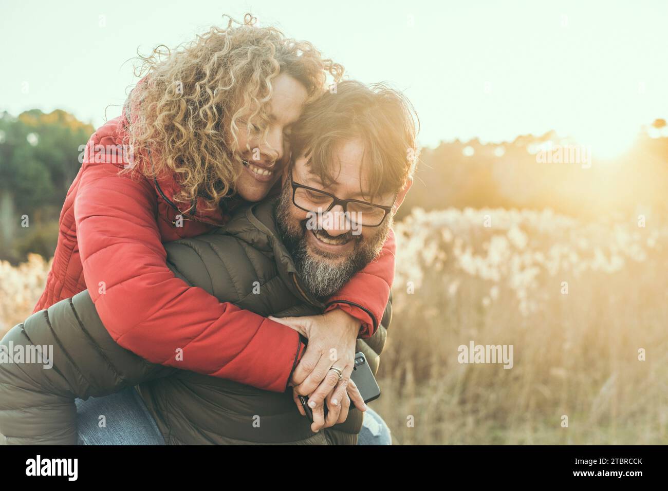 Junges, reifes verliebtes Ehepaar umarmt und lächelt mit romantischem Ausdruck im Gesicht. Ein Mann trägt eine Frau im Huckepack auf dem Rücken. Weibliche Bindung männlich in Outdoor-Freizeitaktivitäten zusammen. Glück Stockfoto