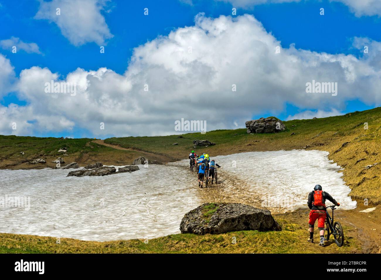 Mountainbiker schieben ihr Mountainbike über ein Schneefeld, Montriond, Chablais, Frankreich Stockfoto
