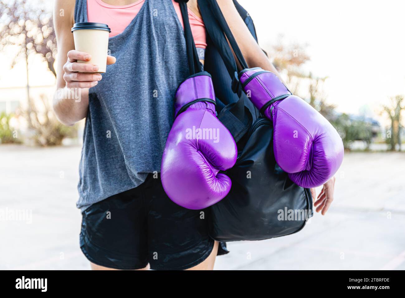 Horizontales Foto von kaukasischen Frauen mit Sportbekleidung, Rucksack, lila Boxhandschuhen und einem Kaffee zum Mitnehmen vor dem Boxstudio. Sport Stockfoto