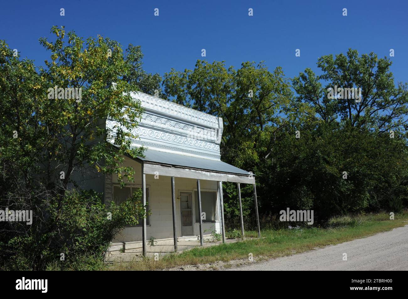 Der alte Landladen an der Feldstraße in Kansas ist wegen Geschäftsarbeiten geschlossen. Die Oberseite des Ladens ist mit dekorativem Zinn bedeckt. Unkraut und Pinsel fangen an, sich zurückzuholen Stockfoto