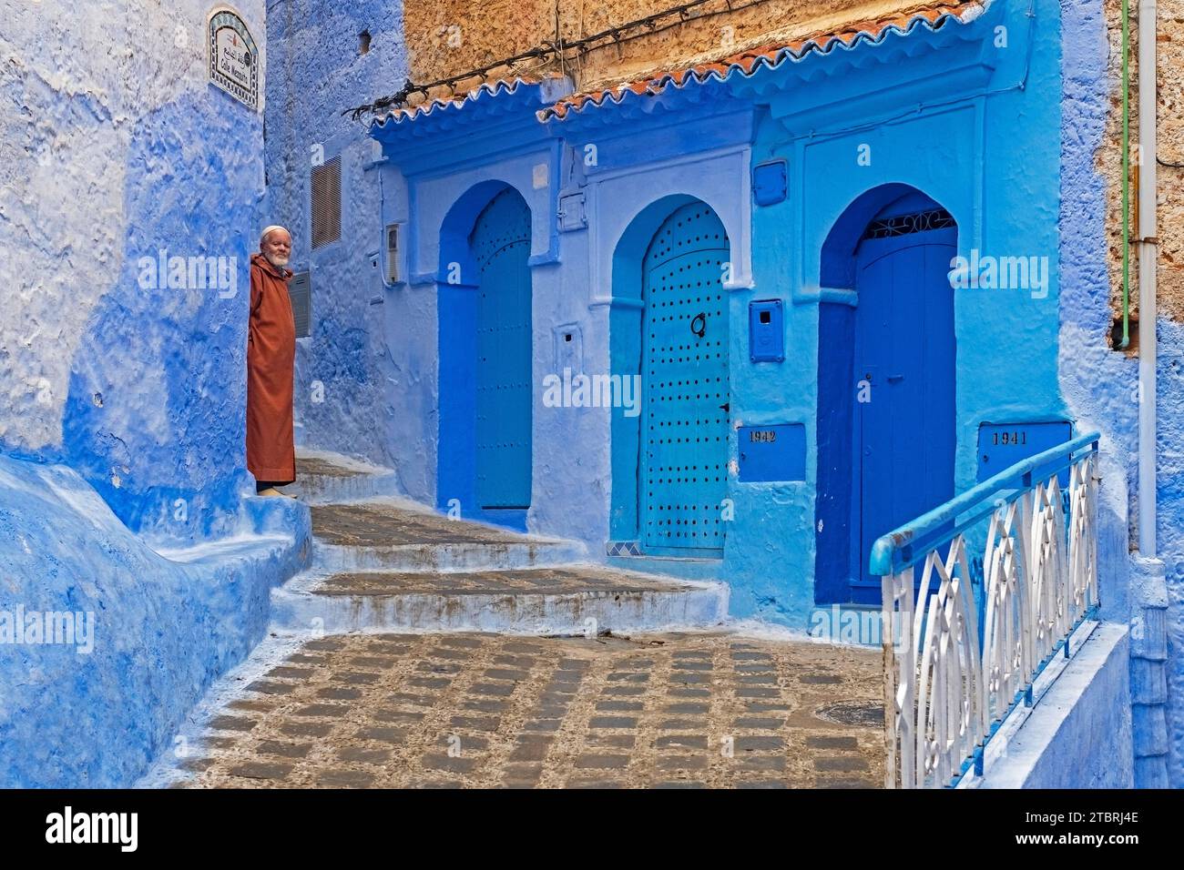 Muslimischer Mann mit traditioneller Djellaba in einer Gasse mit blauen Häusern und Türen in Medina / historischer Altstadt Chefchaouen / Chaouen, Marokko Stockfoto