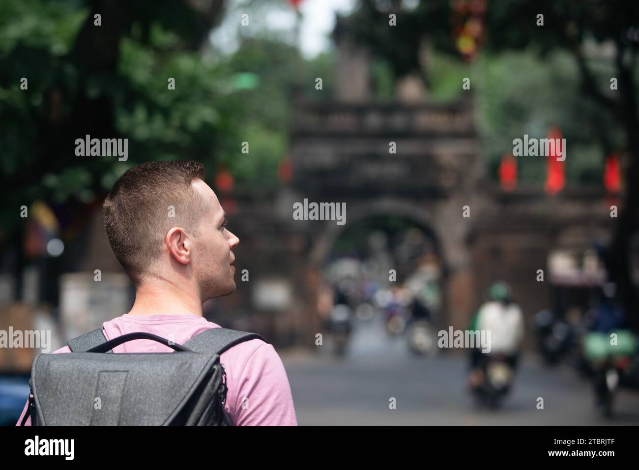 Reisende, die auf einer belebten asiatischen Straße spazieren gehen. Rückansicht eines Mannes mit Rucksack in der Altstadt von Hanoi, Vietnam. Stockfoto