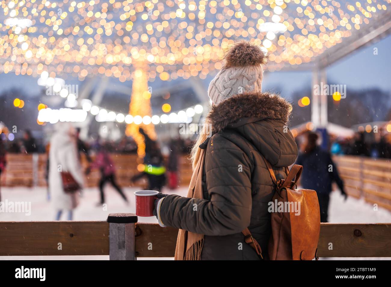 Die Frau sieht eine Menge Leute, die auf der Eisbahn Schlittschuhlaufen und während des 