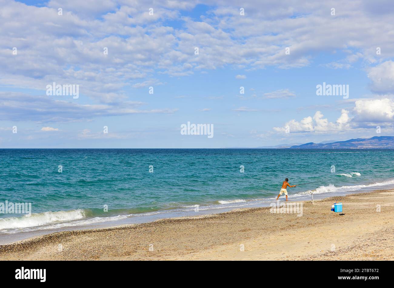 Am Strand Plata Mona, Sardinien, Italien, ist ein sardischer Fischer mit einer Rute abgebildet. Das Bild zeigt den Strand und die fernen Berge. Stockfoto