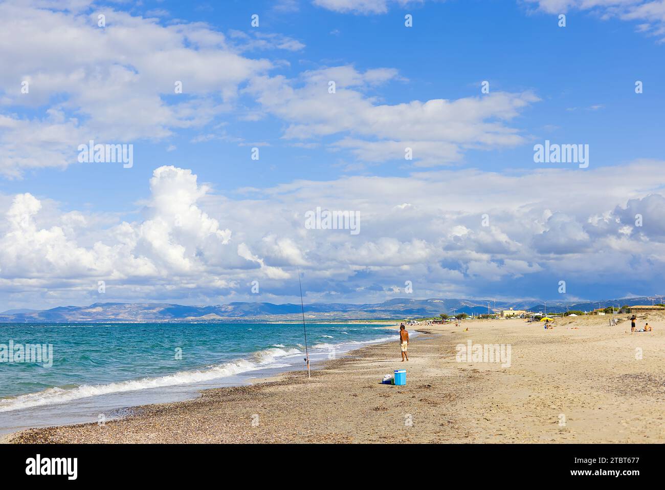 Am Strand Plata Mona, Sardinien, Italien, ist ein sardischer Fischer mit einer Rute abgebildet. Das Bild zeigt den Strand und die fernen Berge. Stockfoto