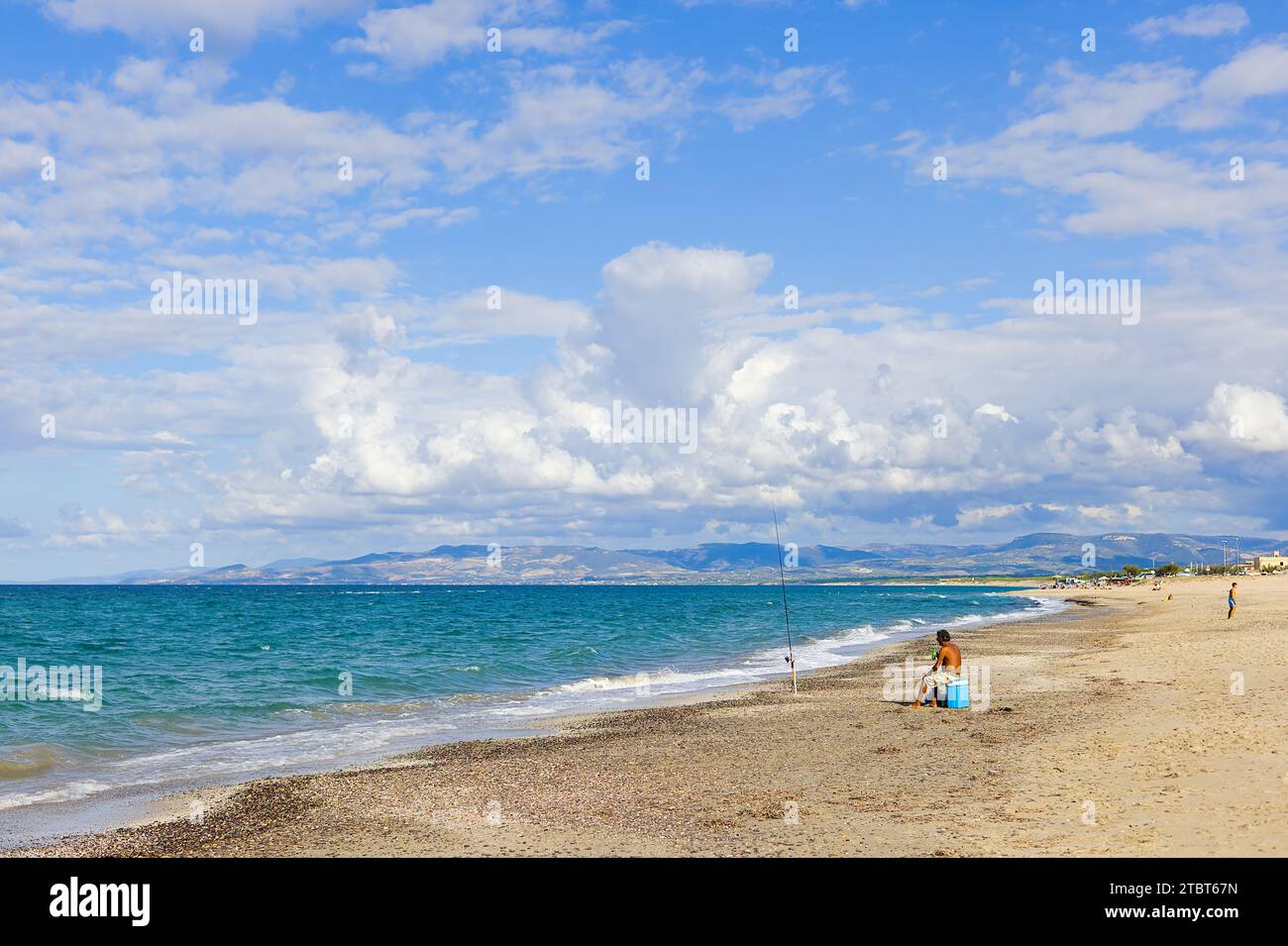 Am Strand Plata Mona, Sardinien, Italien, ist ein sardischer Fischer mit einer Rute abgebildet. Das Bild zeigt den Strand und die fernen Berge. Stockfoto