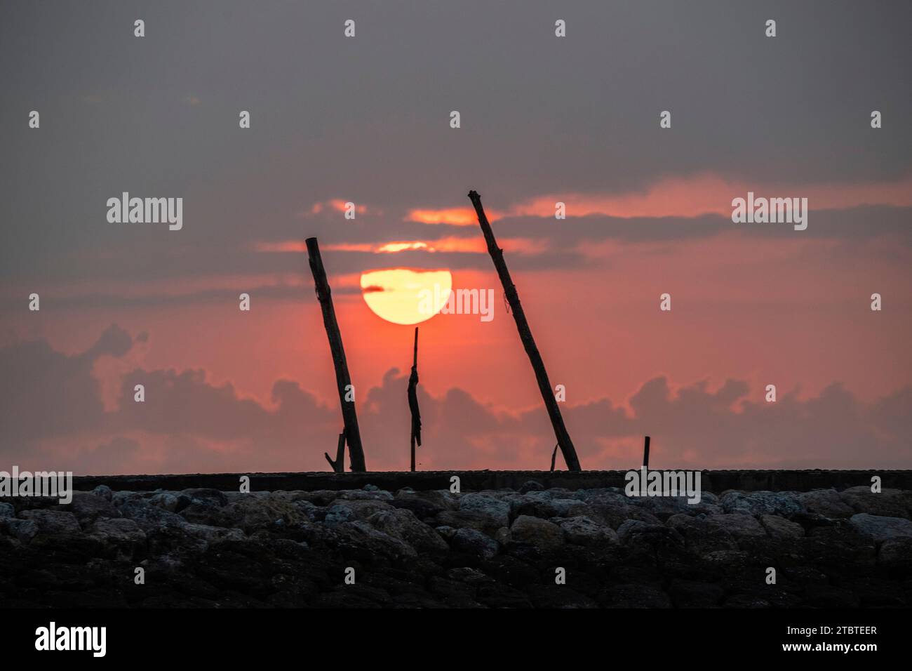 Sonnenaufgang am Sandstrand mit kleinen Tempeln im Wasser, Landschaft mit roter kreisförmiger Sonne am Strand von Sanur, Bali, Indonesien Stockfoto