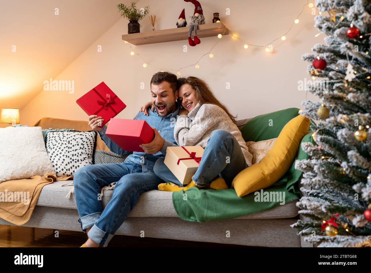 Saison des Gebens. Glücklicher Mann überrascht, sein Weihnachtsgeschenk zu erhalten. Junge Paare in den Weihnachtsferien. Stockfoto