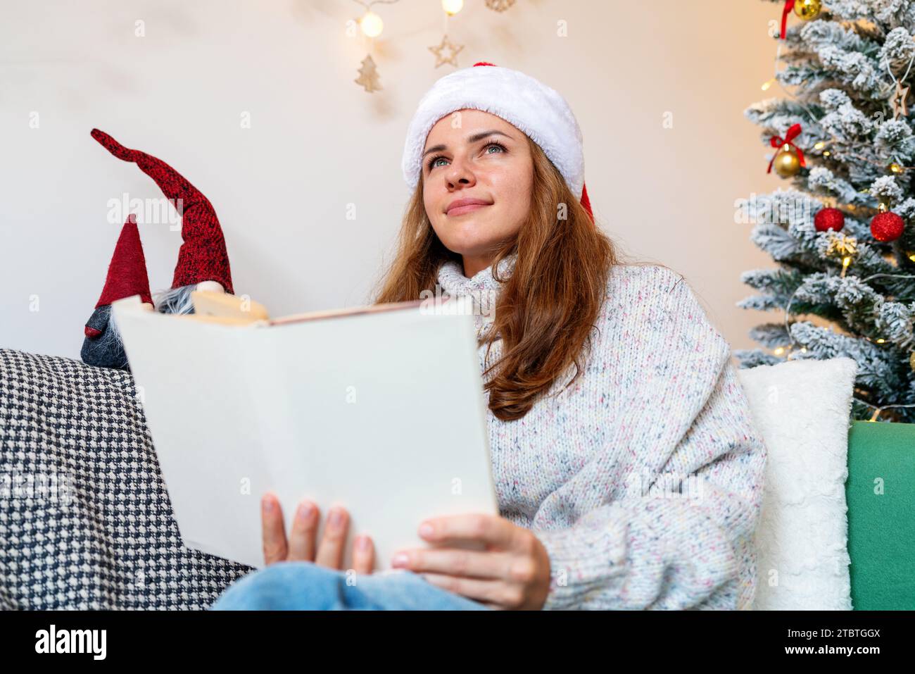 Erwachsene Frau mit Weihnachtsmütze, die Märchenbuch, Fantasien und Träume während der Weihnachtsferien liest. Stockfoto