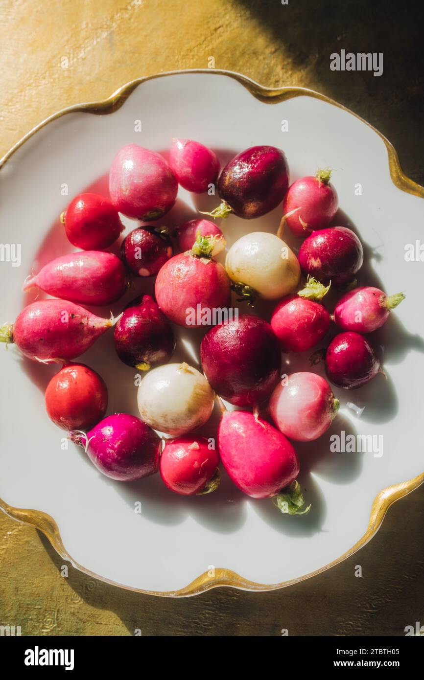 Eine Auswahl von getrimmten rosa, roten, lila, weißen Radieschen auf weißem Teller mit goldenem Rand und Rand Stockfoto