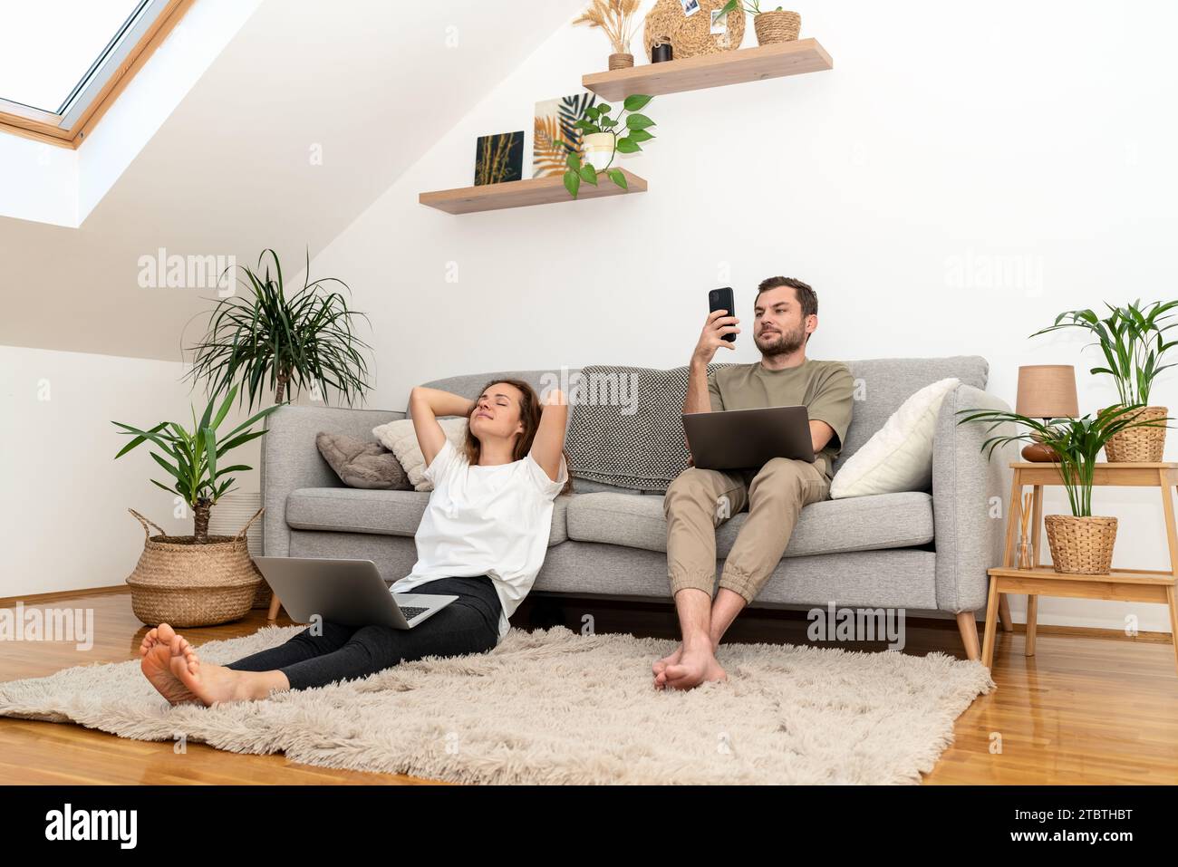 Junge Paare zu Hause mit ihren Laptops und Smartphones... Tragbare Informationsgeräte und der Lebensstil von Menschen im Haushalt. Stockfoto