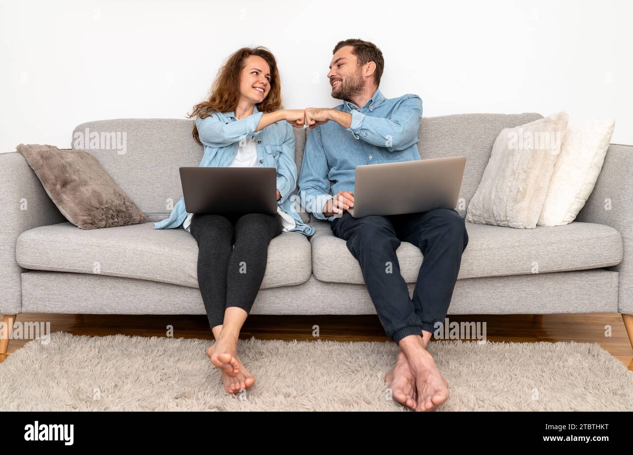 Ein Paar, das zu Hause an Laptops arbeitet und Faustschläge macht. Gegenseitiges Verständnis und Teamarbeit in der Familie. Stockfoto